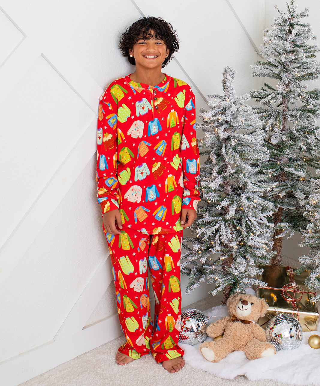Person wearing red pajamas with colorful patterns, standing next to a decorated Christmas tree.