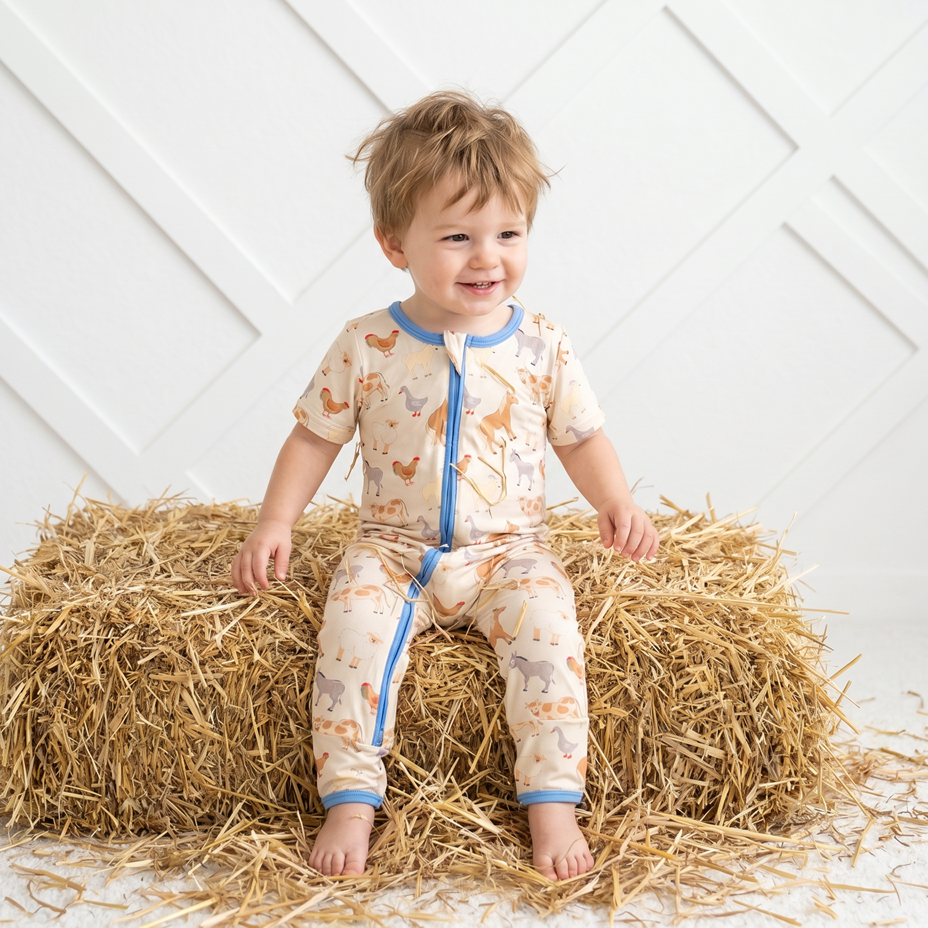 Child wearing a patterned onesie sitting on a bale of hay against a white wall.
