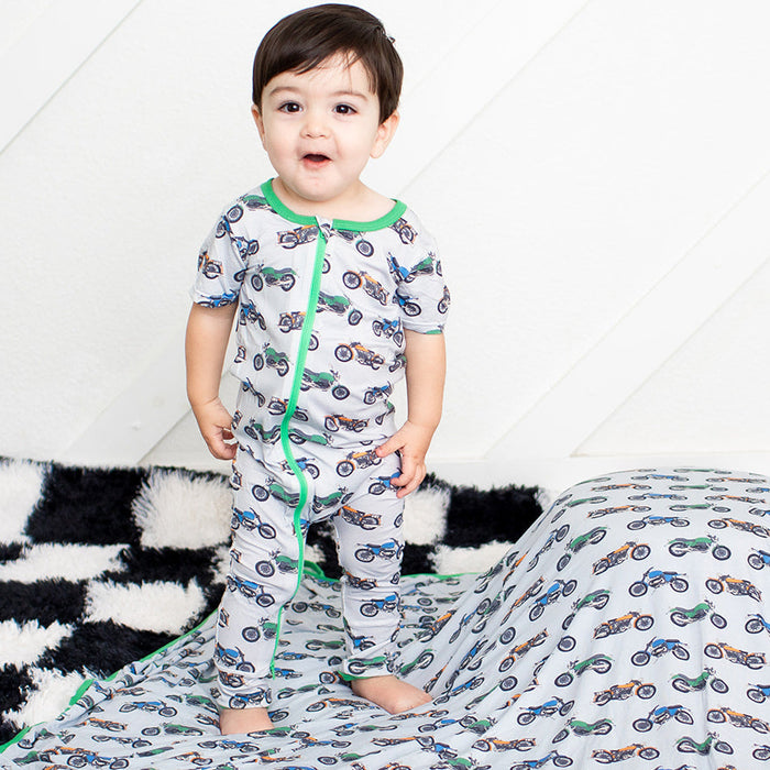 Child playing with a large blanket featuring car patterns on a checkered floor.
