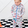 Child wearing a patterned onesie on a checkered rug with toys and a cone.