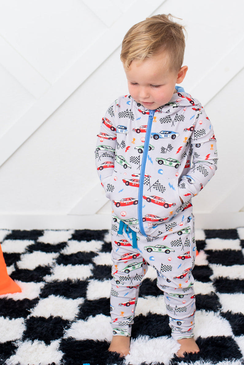 Child wearing a patterned onesie on a checkered rug with toys and a cone.