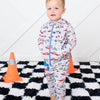 Child wearing a onesie with car pattern on a checkered floor with traffic cones.
