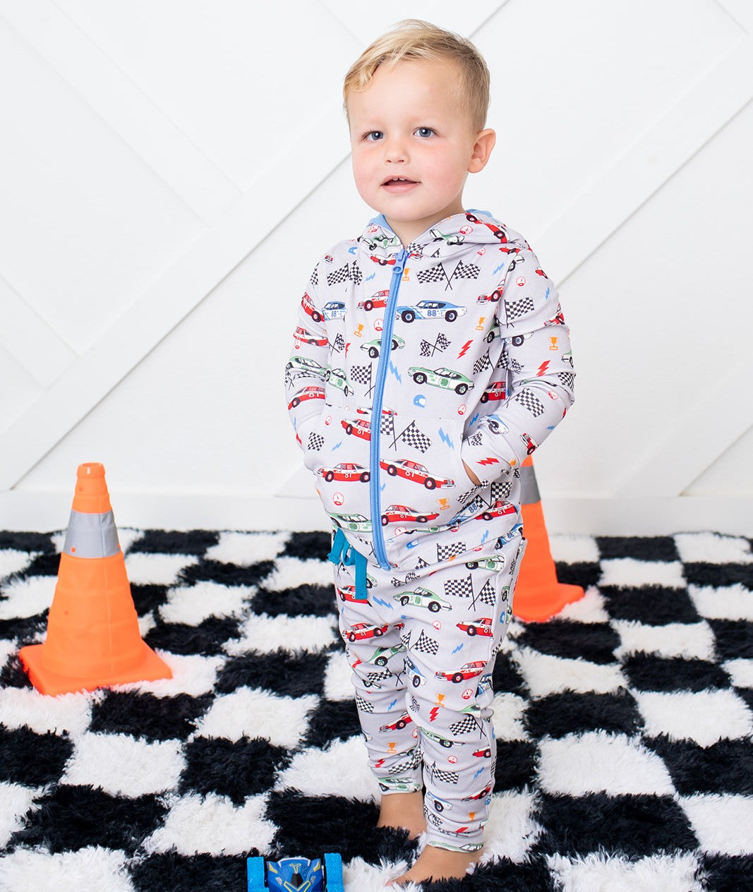 Child wearing a onesie with car pattern on a checkered floor with traffic cones.