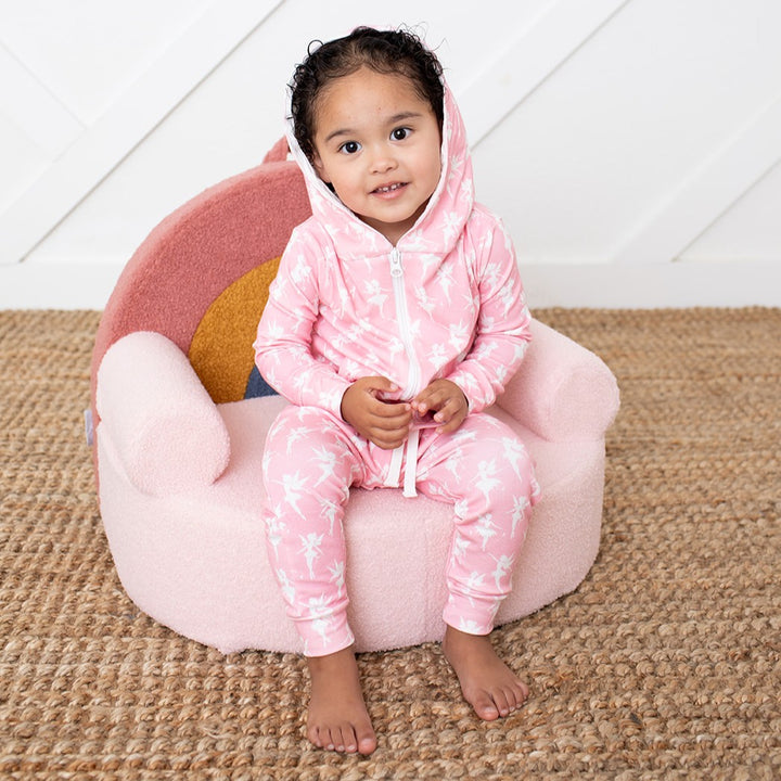 Child wearing a pink onesie with white patterns, sitting on a pink bean bag chair.