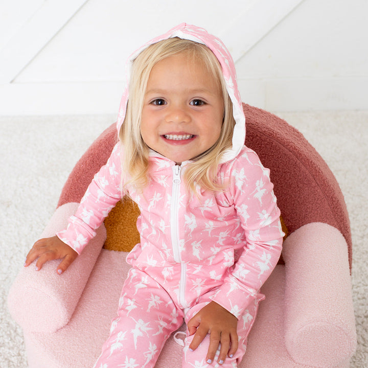 Child wearing a pink onesie with white patterns, sitting on a pink cushion.