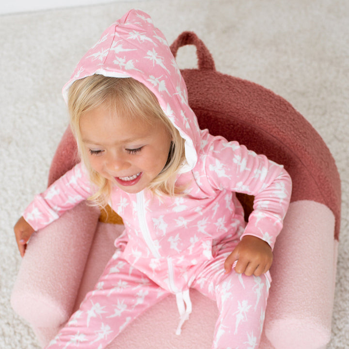 Child wearing a pink onesie with white patterns, sitting on a pink cushion.