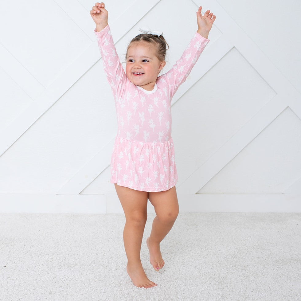 Child wearing a pink tie-dye dress with arms raised on a white background