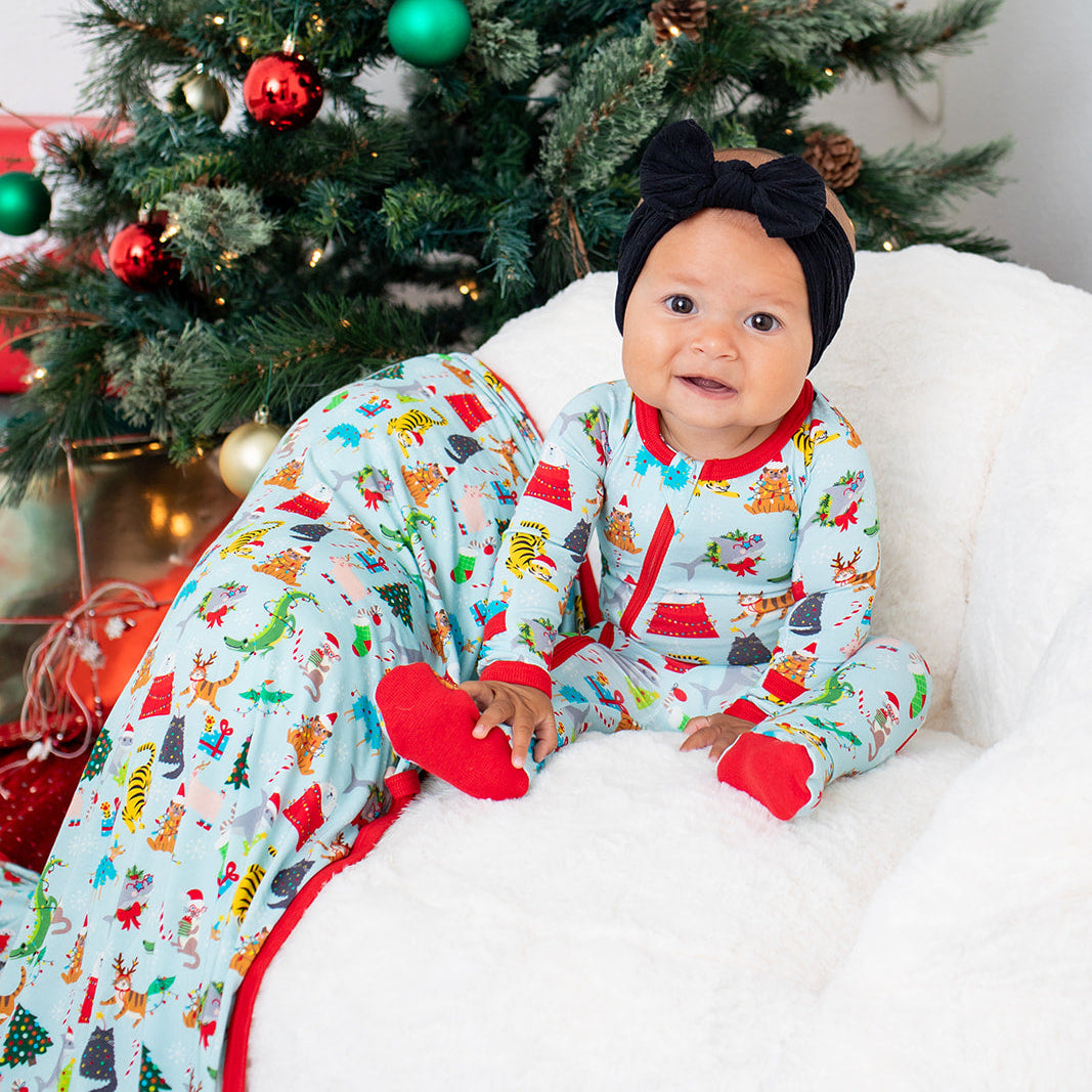 Baby in festive pajamas sitting in front of a decorated Christmas tree.