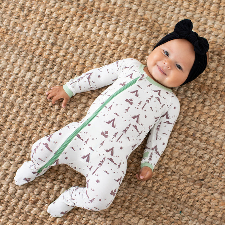 Baby lying on a carpet wearing a patterned onesie with a green zipper.