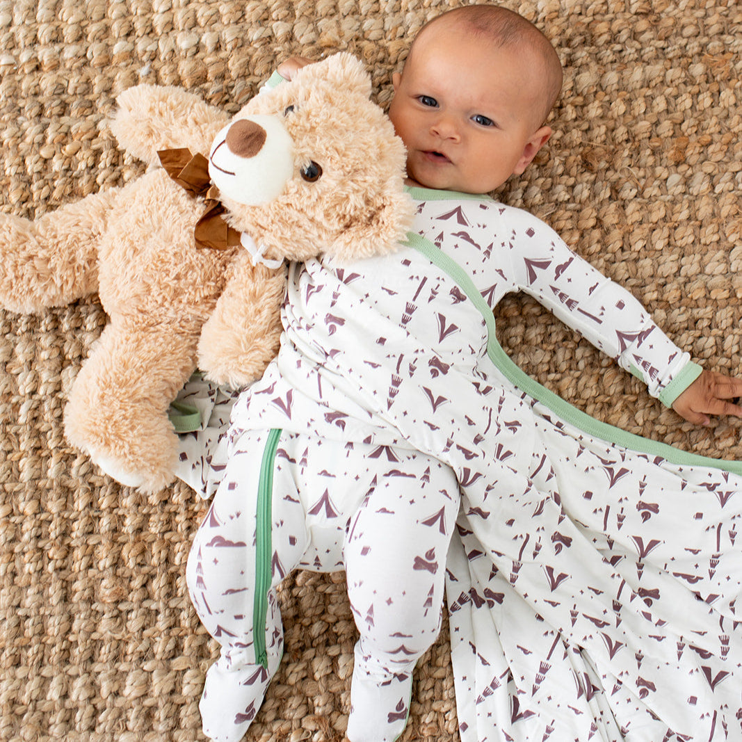 Baby lying on a textured surface with a teddy bear and patterned blanket