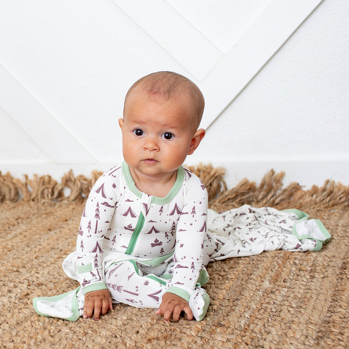 Baby sitting on a textured rug wearing a patterned onesie.