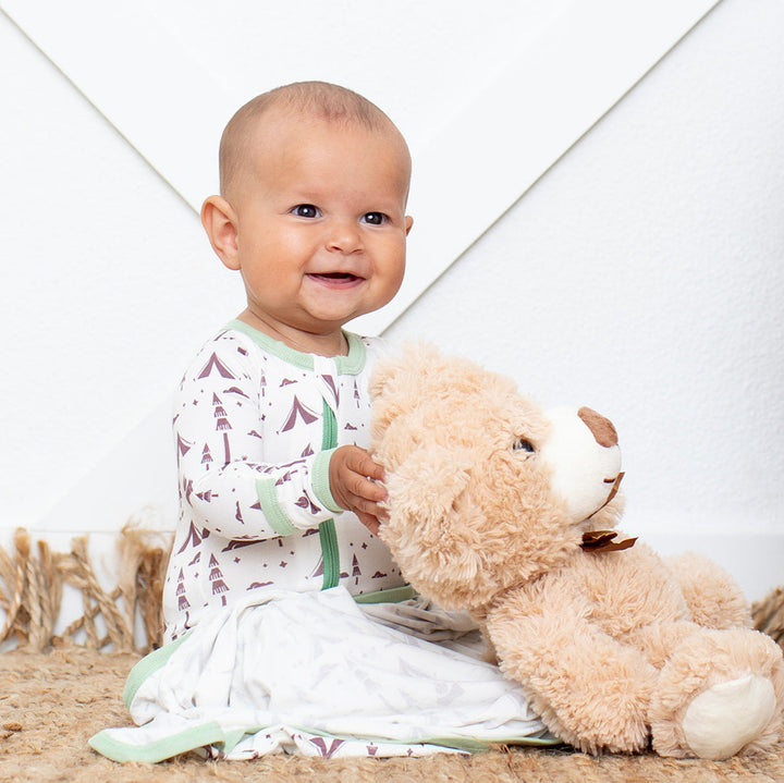Baby holding a teddy bear in a room with a white wall and wooden elements.