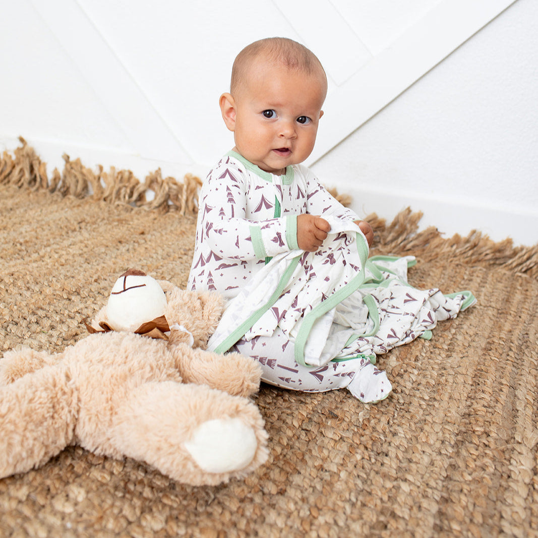 Baby sitting on a textured surface with a teddy bear, wearing a patterned outfit.