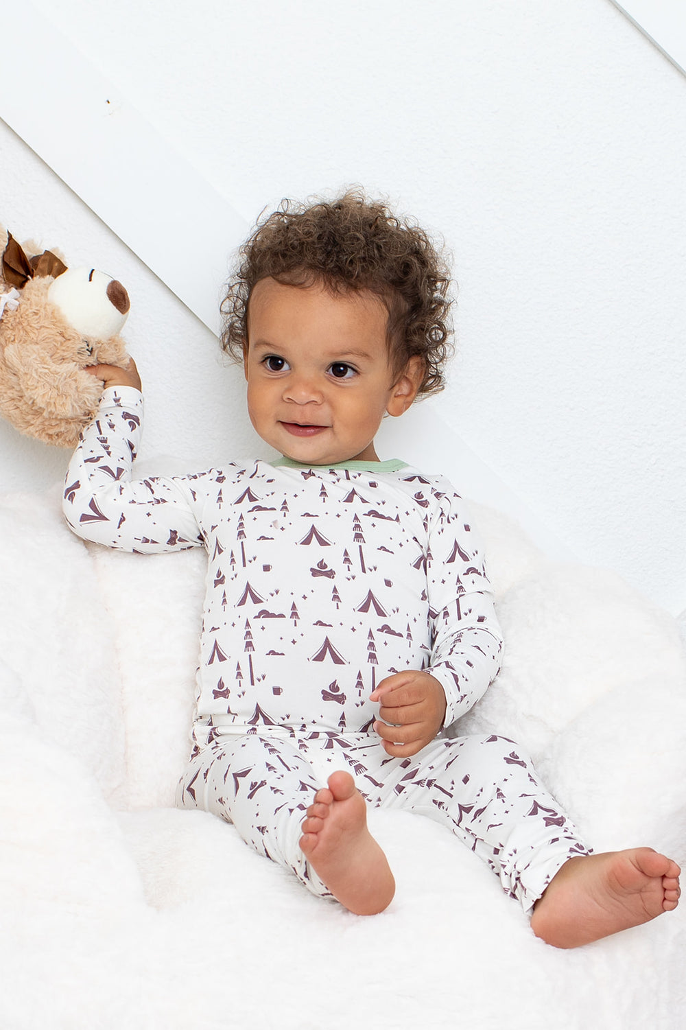Baby wearing a white onesie with brown animal prints, holding a plush toy on a white background