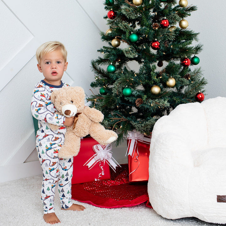 Child holding a teddy bear next to a decorated Christmas tree and white bean bag chair.