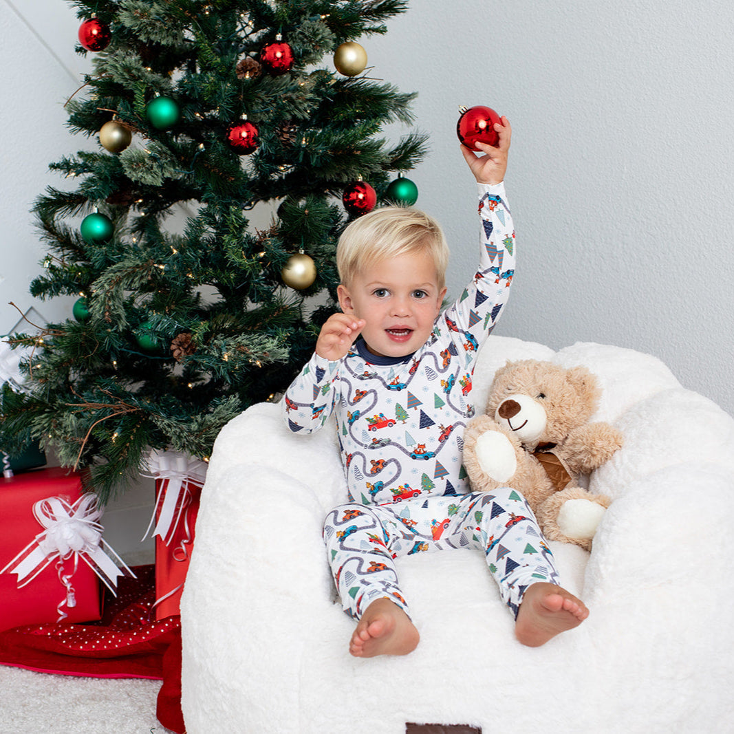 Child in pajamas sitting on a bean bag with a Christmas tree and presents in the background