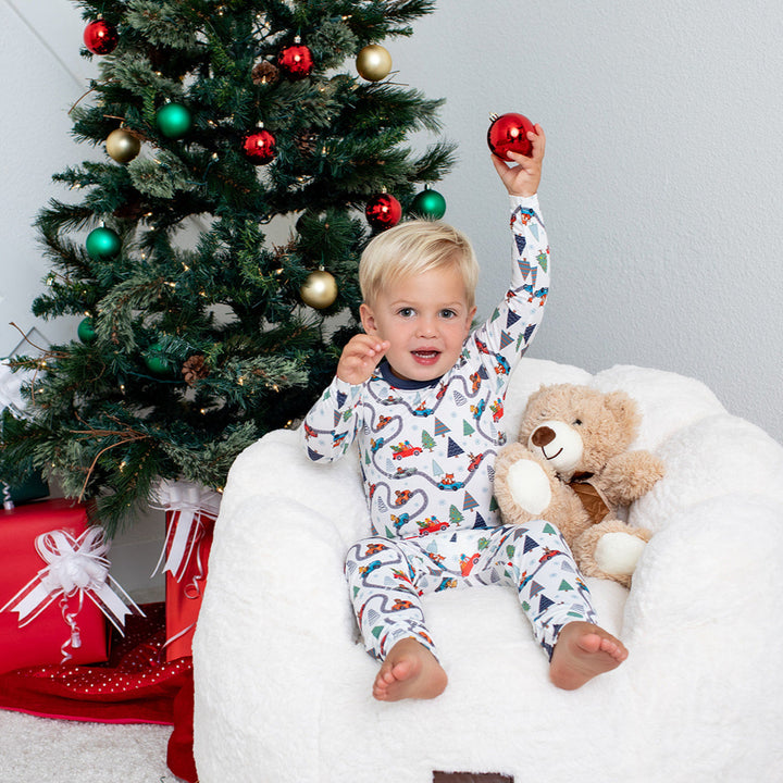 Child in pajamas sitting on a bean bag with a Christmas tree and presents in the background