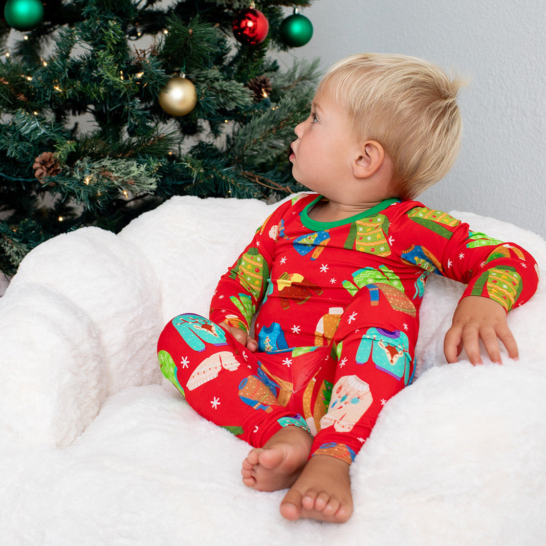 Child in festive pajamas sitting on a bean bag chair next to a decorated Christmas tree with presents.