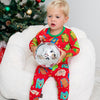 Child in festive pajamas holding a disco ball in front of a decorated Christmas tree.