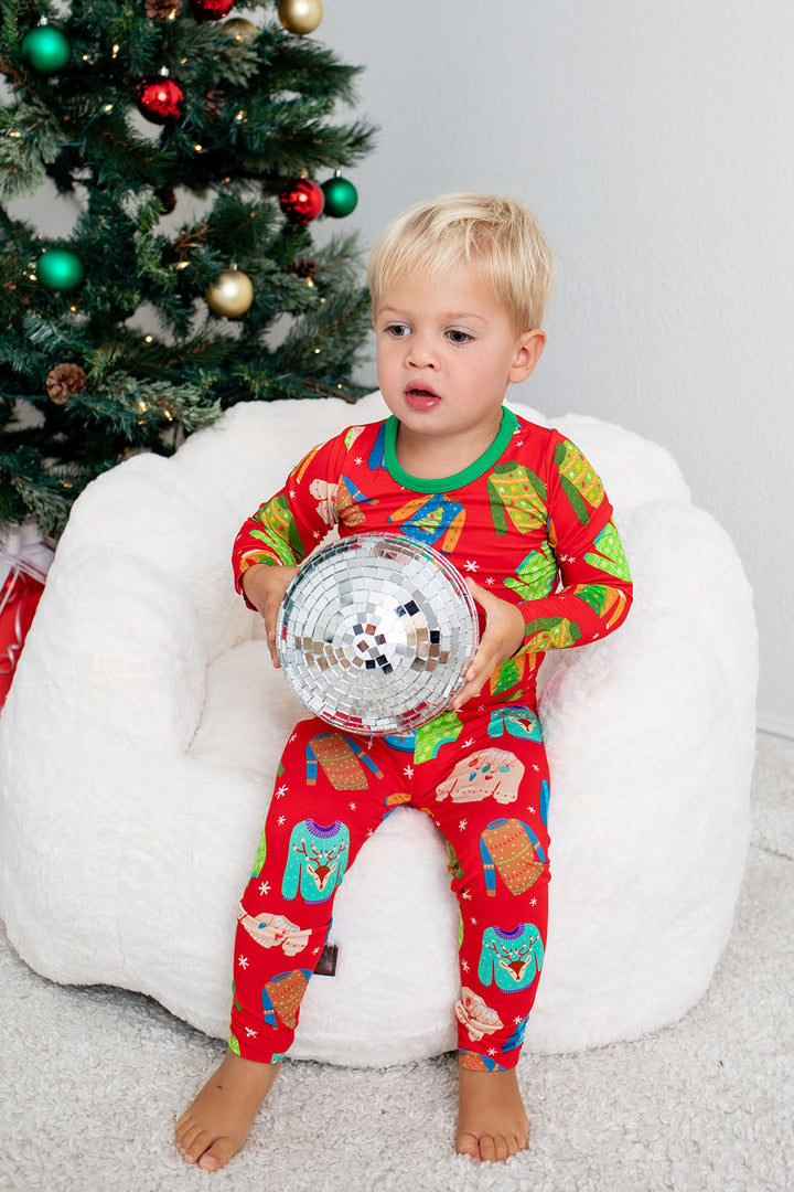 Child in festive pajamas holding a disco ball in front of a decorated Christmas tree.