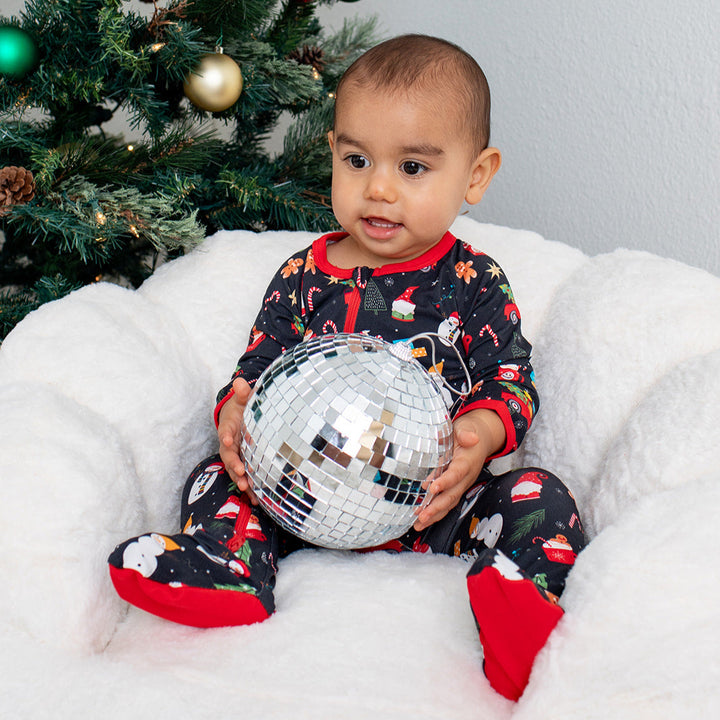 Child holding a disco ball in front of a decorated Christmas tree