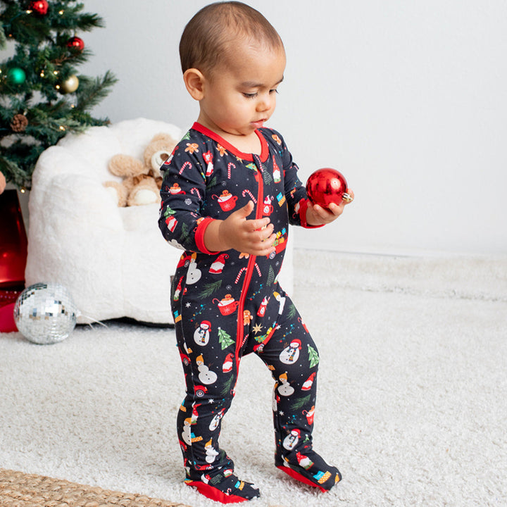 Two children in Christmas-themed pajamas standing near a decorated Christmas tree and presents.
