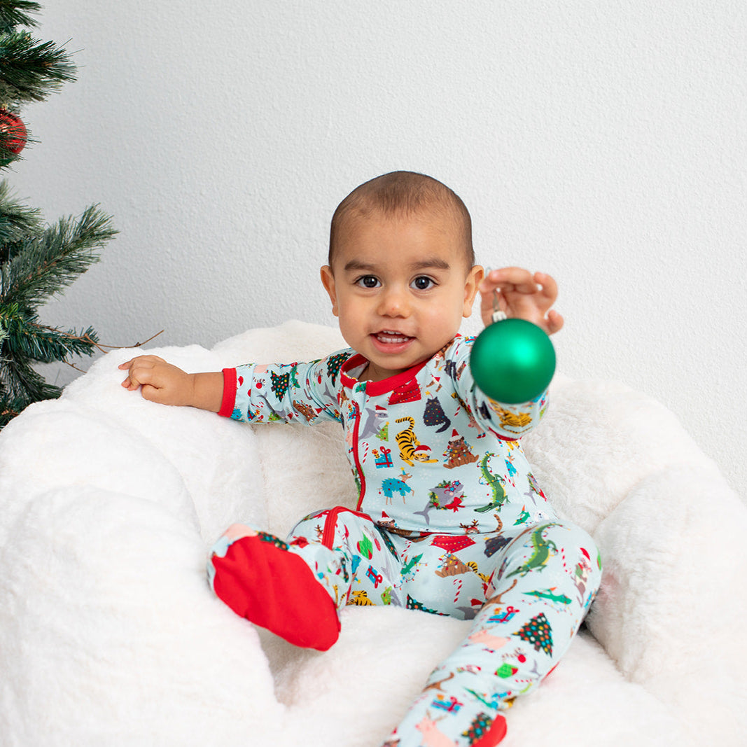 Baby in pajamas holding a green ornament with a Christmas tree in the background