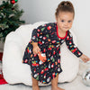 Child in a festive dress sitting on a white chair with Christmas decorations in the background.