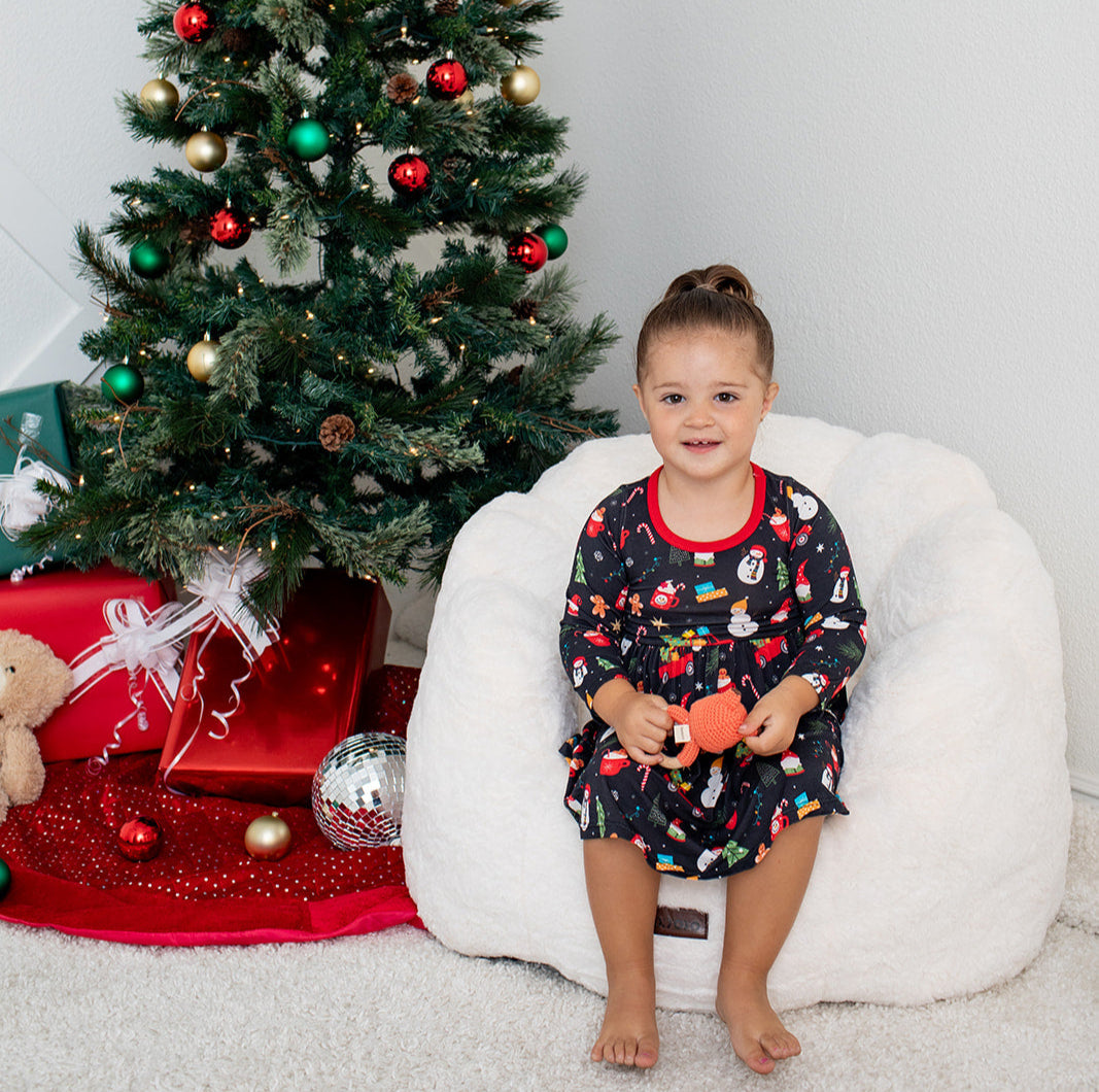 Child in pajamas sitting on a bean bag chair next to a decorated Christmas tree.