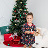 Child in a festive outfit standing in front of a decorated Christmas tree with presents.