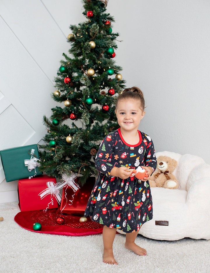 Child in a festive outfit standing in front of a decorated Christmas tree with presents.