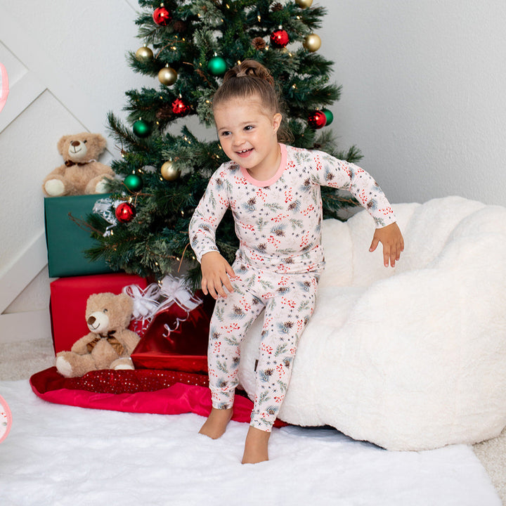 Child in pajamas standing next to a decorated Christmas tree with presents underneath.