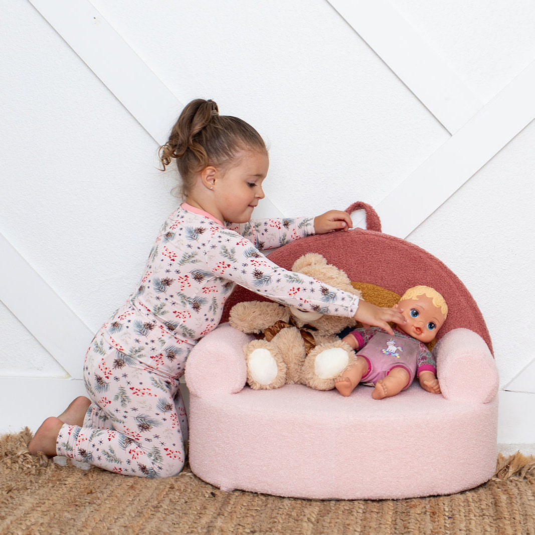 Child playing with stuffed toys inside a pink bean bag chair against a white wall.