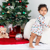 Child in pajamas standing next to a decorated Christmas tree with presents and toys.