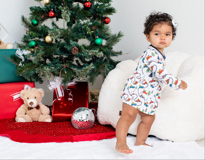 Child in pajamas standing next to a decorated Christmas tree with presents and toys.