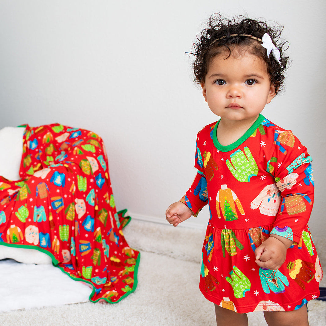 Child wearing a red Christmas-themed outfit with a decorated tree in the background