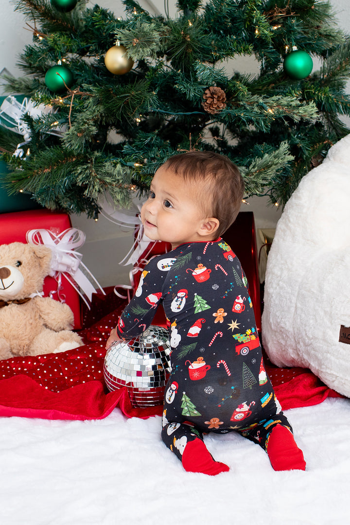 Child in festive pajamas sitting in front of a decorated Christmas tree with presents and a teddy bear.
