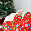 Baby in a colorful outfit sitting next to a Christmas tree with decorations and presents.