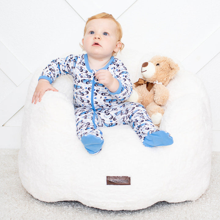 Baby sitting on a bean bag with a teddy bear on a white background