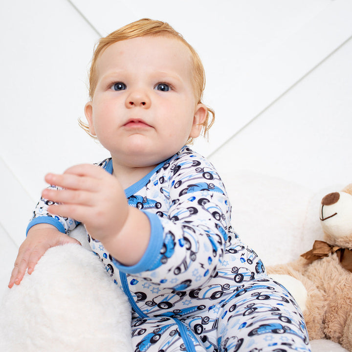 Baby in a patterned onesie sitting on a white surface with a teddy bear.