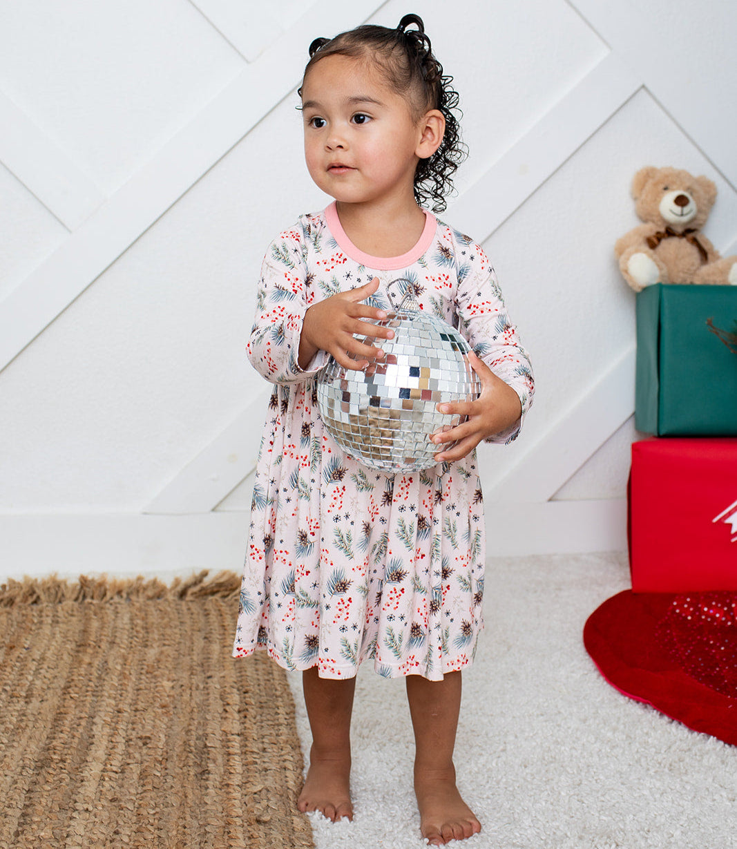 Child holding a disco ball in a room with a teddy bear and gift box in the background