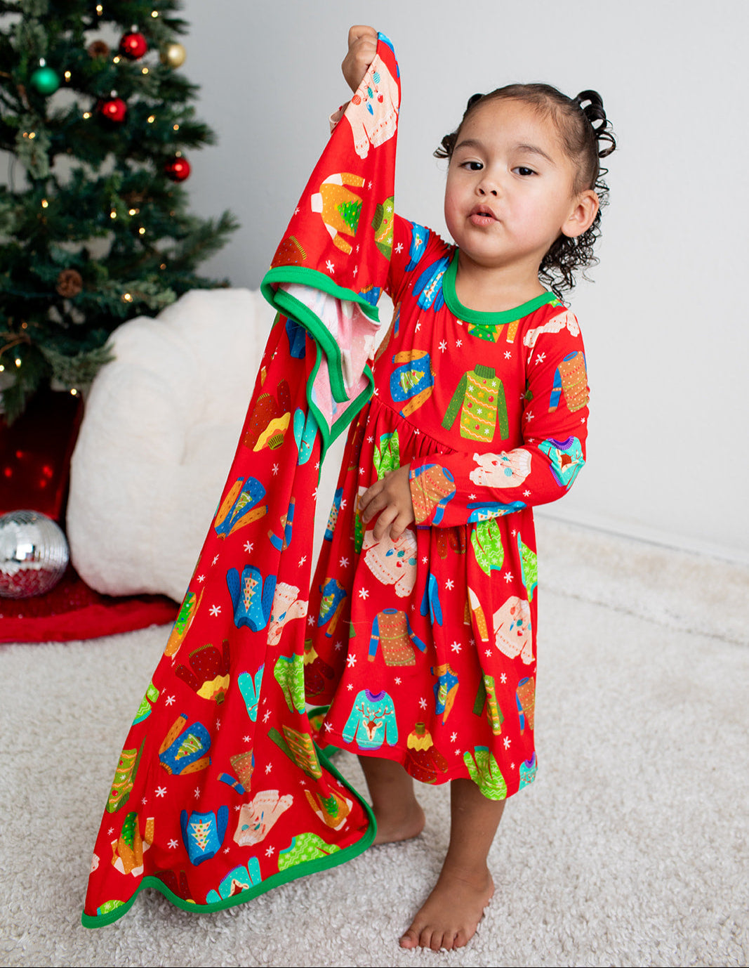 Child wearing a red holiday-themed dress with a Christmas tree in the background
