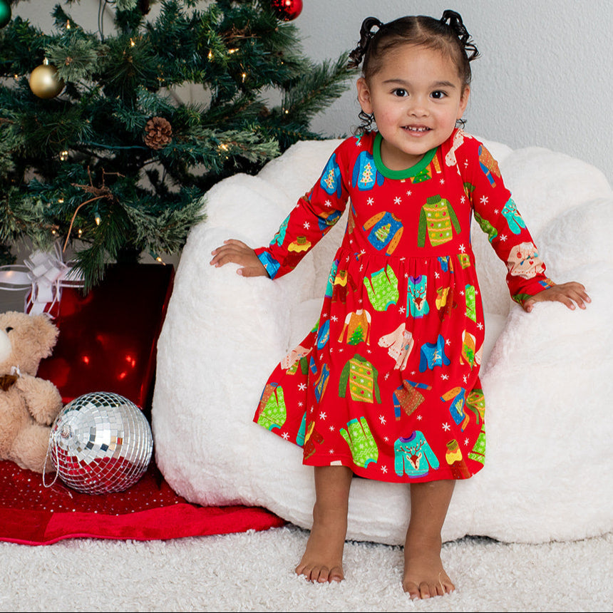 Child in a red Christmas-themed pajama sitting on a white bean bag chair next to a decorated Christmas tree.