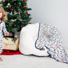 Child in pajamas holding a teddy bear in front of a Christmas tree with presents.