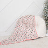 Small Christmas tree with decorative items next to a white ottoman with a floral blanket