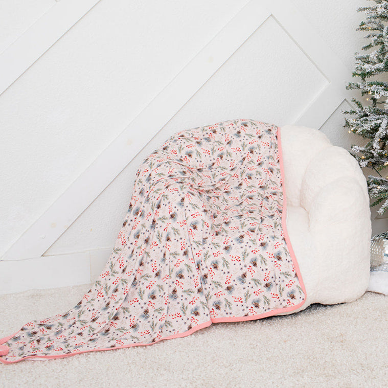 Small Christmas tree with decorative items next to a white ottoman with a floral blanket