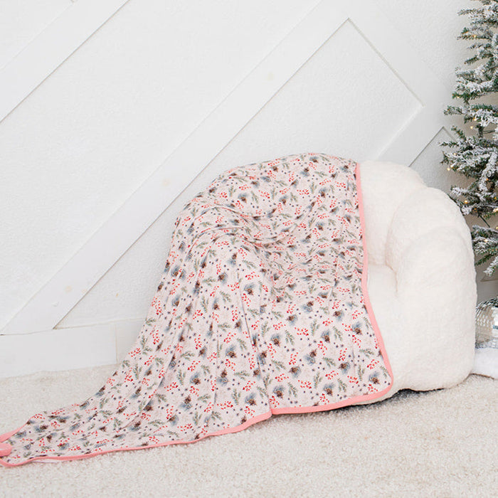Small Christmas tree with decorative items next to a white ottoman with a floral blanket