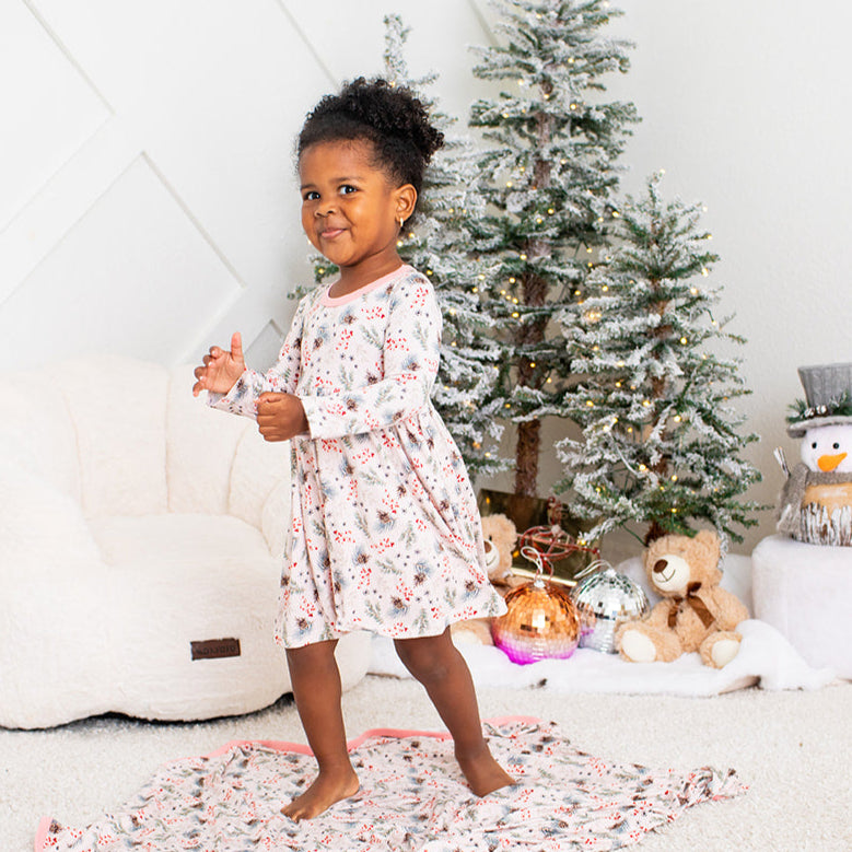 Child in a floral dress standing in front of a Christmas tree with presents underneath.