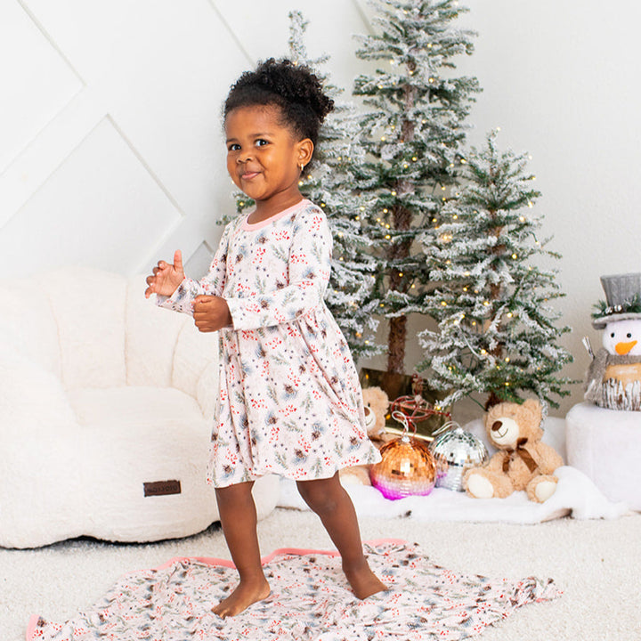 Child in a floral dress standing in front of a Christmas tree with presents underneath.
