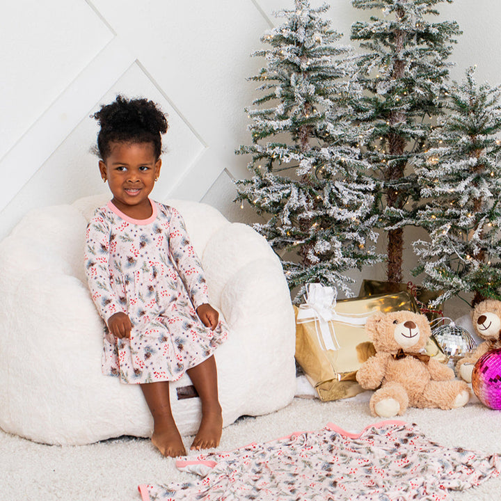 Child in a floral dress sitting on the floor with Christmas decorations including a tree and presents.